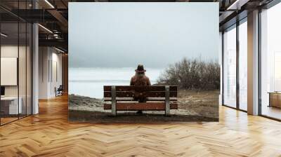 Fashionable woman sitting on bench looking out at lake Wall mural