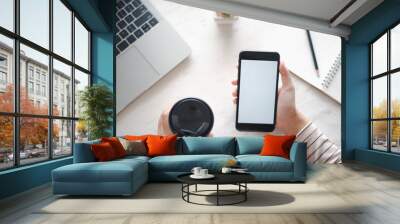 Closed up and focus on hand of young woman using a smartphone which show white display other hand hold a cup of coffee and have notebook put on table in near. see top view. co working space concept. Wall mural