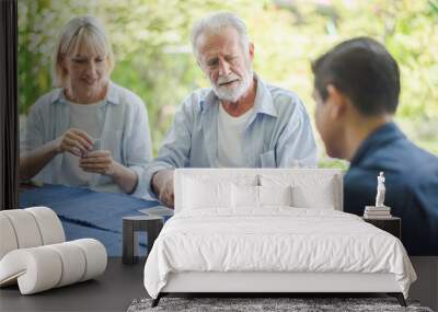 Group of positive seniors European and Asia are playing card game on the table outdoor at retirement home. Retired people are playing card having fun to enjoying and smiling felling happy. Wall mural