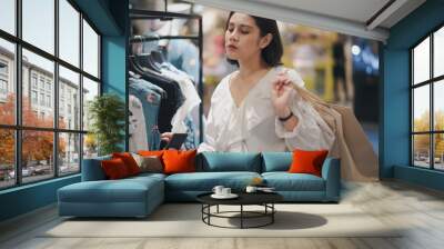 Young Asian beautiful woman shot hair smiling shopping new clothes in a shopping mall store. Woman standing and holding a shopping bag and in the store. Wall mural