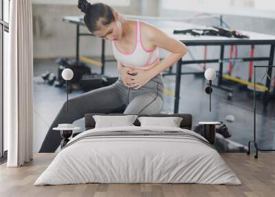 Young Woman have stomach ache while workout at gym which background is table tennis. Accident weight training at fitness, muscle pain concept. Wall mural