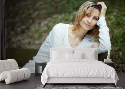 Portrait of smiling woman sitting on a bench in a park Wall mural