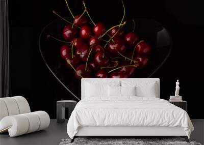 Cherries on black plate in form of heart. Cherry berry on a black background. Dark image of red cherries on a black reflective surface. Wall mural