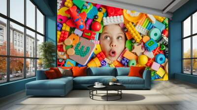 Funny surprised little girl lying in the chaos of toys Wall mural