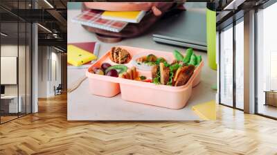 Open lunch box with healthy food on the table near backpack, laptop and thermo mug Wall mural