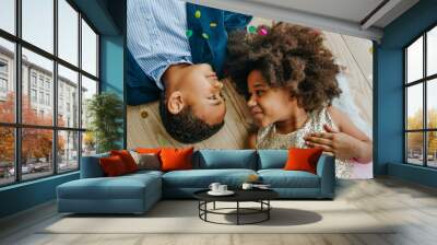 Two happy boy and girl lying on the floor under flying confetti Wall mural