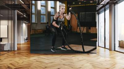 Young woman training with battle ropes at gym Wall mural