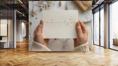 Woman's hands holding a white card with gold confetti design. Wall mural