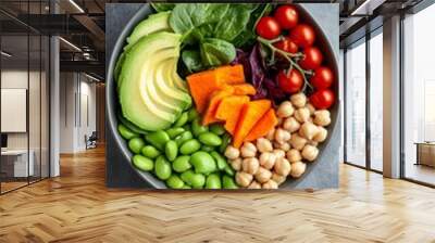 A vibrant bowl of fresh vegetables, avocado, and sweet potato with chickpeas for an eco-friendly meal on a gray background. The photo showcases the colorful arrangement of organic ingredients  Wall mural