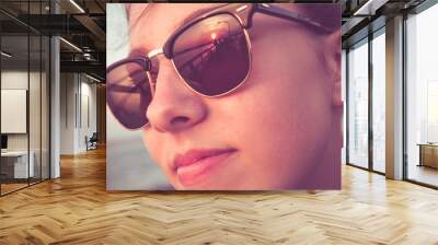 Vintage toned close-up face of a beautiful young teenage girl at beach with reflection of sunset in her sunglasses  Wall mural