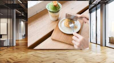 Close-up of a woman eating a green tea cake with a fork and knife at a wooden table Wall mural