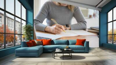 Student sitting at table and writing on notebook. Young female student studying at cafe Wall mural