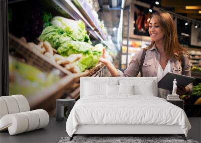 Beautiful woman buying vegetables healthy food in supermarket. Shelves full of green food. Wall mural