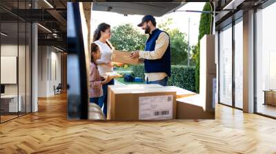 Courier delivering packages with toys to the woman and little girl. Wall mural