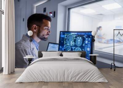 Doctor examining X-ray images on display in MRI control room while in background nurse preparing the patient for examination test. Wall mural