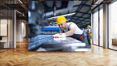 Factory worker in protective uniform and hardhat operating industrial machine at production line. People working in industry. Wall mural