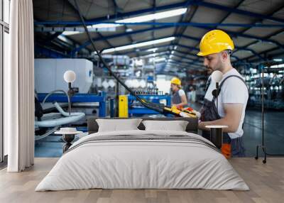 Factory worker wearing uniform and hardhat operating industrial machine with push button joystick in production hall. Employee working on industry production machine. Wall mural