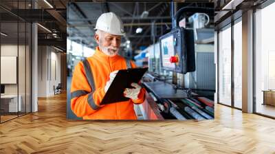 Industrial worker in safety visible uniform and hardhat inspecting process of production and machine operations in factory. Wall mural