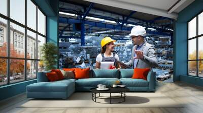 Manager wearing hardhat and industrial worker discussing about production in metal factory. Positive people talking about business. Wall mural