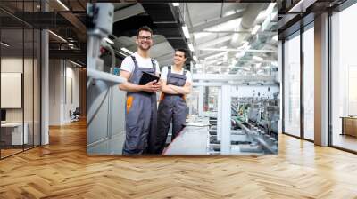 Portrait of production line workers controlling manufacturing process of modern packaging industrial machine in printing factory. Wall mural