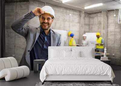 Portrait of smiling caucasian civil engineer holding project plans at construction site. Wall mural