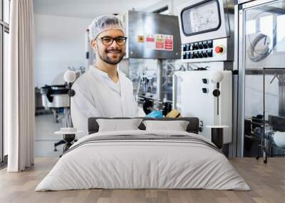 Portrait of technologist or worker in sterile white clothing standing by automated industrial machine in pharmaceutical company or factory. Wall mural