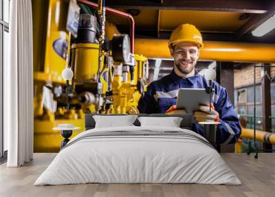 Power plant engineer in safety work wear standing by natural gas installations and pipeline checking consumption on tablet computer application. Wall mural