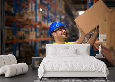 Working at warehouse. Smiling warehouse worker moving boxes on the shelf. Wall mural