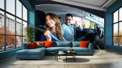 Young smiling couple testing new car and wearing seat belts on. Car safety. Wall mural