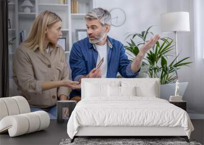 A mature couple engages in a heated discussion about online credit card fraud, gesturing at a laptop and credit card in a modern living room. Wall mural