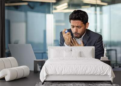 Arab businessman suffering from asthma in modern office, young man holding inhaler in hand and holding chest, breathing hard, breathing and health problems Wall mural