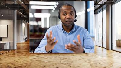 Businessman using headset participates in video call discussing projects. Focused expression suggests in-depth conversation. Modern workspace visible, emphasizing professional setting. Wall mural