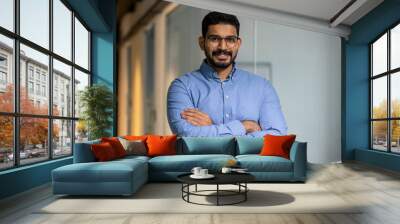 Businessman with crossed arms smiling and looking at camera, portrait of happy male worker inside office, boss in glasses and shirt, happy with achievement results, proud and confident. Wall mural