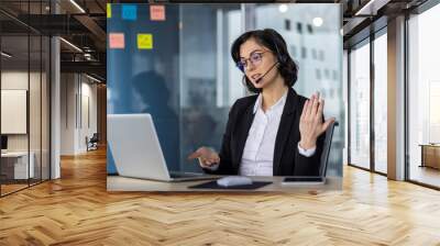 Businesswoman wearing headset on video call in modern office, discussing serious topics. Office background with sticky notes. Technology and communication in professional work environment. Wall mural