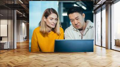 Close-up photo, a team of 2 office workers, an Asian man and a woman looking at a computer monitor Wall mural