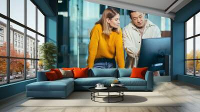 Close-up photo, a team of 2 office workers, an Asian man and a woman looking at a computer monitor Wall mural