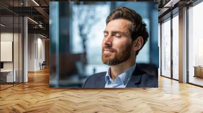 Close-up photo. Portrait of a handsome young man who closed his eyes and rests at the workplace. Sitting relaxed in the office. Wall mural