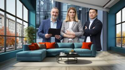 Diverse team man and woman outside office building business people with crossed arms looking thoughtfully at camera colleagues employees three persons Wall mural