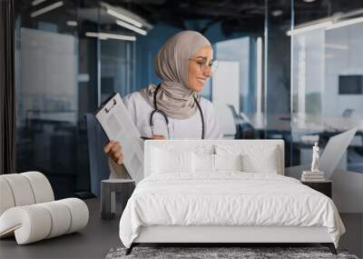 Doctor online consultation with patient, muslim woman in hijab working remotely with laptop for video call, consulting patients sitting inside modern clinic office Wall mural