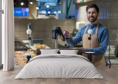 Grocery store employee in blue shirt and apron weighing fresh meat in delicatessen section. Smiling and engaging with customers, utilizing modern digital scale for accuracy Wall mural