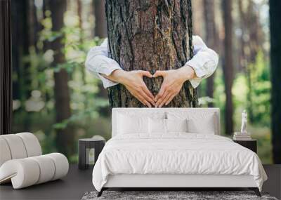 hands of a young woman hug a tree in the forest and show a sign of heart and love for nature Wall mural