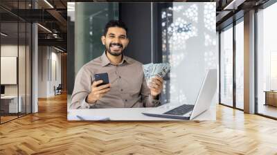 Happy businessman holding cash and phone in modern office setting Wall mural