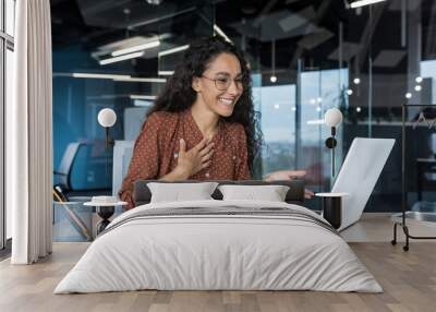 Happy hispanic businesswoman working in modern office using laptop for video call and online meeting with fellow employees, woman smiling and having fun giving a presentation Wall mural