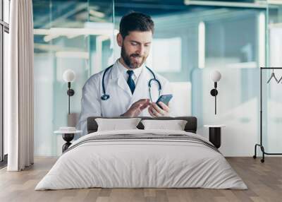 Male doctor in a white coat in a modern clinic reads information from a mobile phone corresponds with colleagues happy and smiles Wall mural