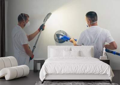 Plasterer smoothes the wall surface with a wall grinder. Two master builders grind a white plaster wall. a man in overalls grinds the surface in a respirator. experienced repairman Wall mural