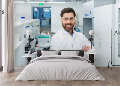 Portrait mature experienced laboratory assistant in a small laboratory, a man with a beard and glasses is smiling and looking at the camera among microscopes, a scientist in a white medical coat Wall mural