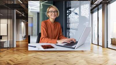 Portrait of happy and successful female programmer inside office at workplace, worker smiling and looking at camera with laptop blonde businesswoman is satisfied with results of achievements at work Wall mural