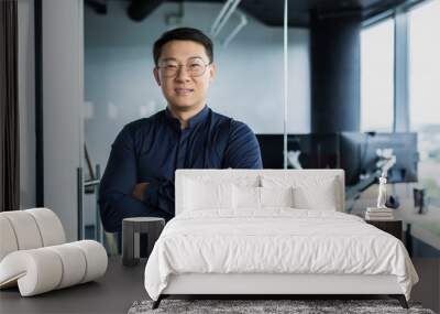 Portrait of successful Asian programmer, team leader company owner smiling and looking at camera with crossed arms, talented startup entrepreneur working inside IT office Wall mural