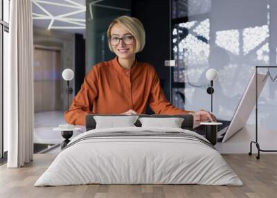 Portrait of successful financier woman, businesswoman behind paper accounting work smiling and looking at camera, female worker happy at workplace using laptop inside office, blonde in glasses. Wall mural