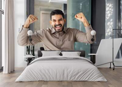 Portrait of winner businessman at workplace, man with laptop is happy looking at camera, holding hands up, gesture of success, satisfied with achievement results Wall mural